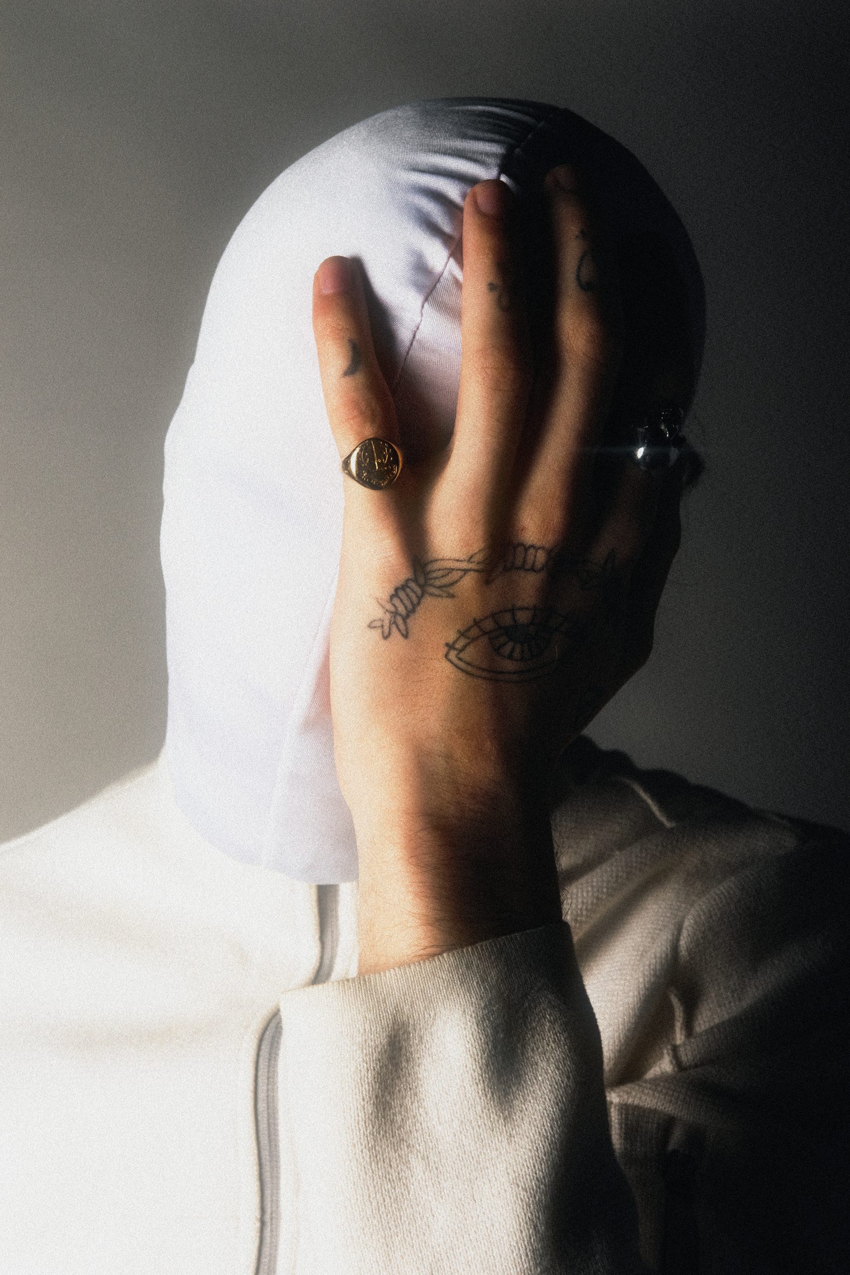 Brièveté n'est pas vitesse, photo de l'artiste rappeur NZ en blanc, portant une cagoule blanche avec un main sur le visage