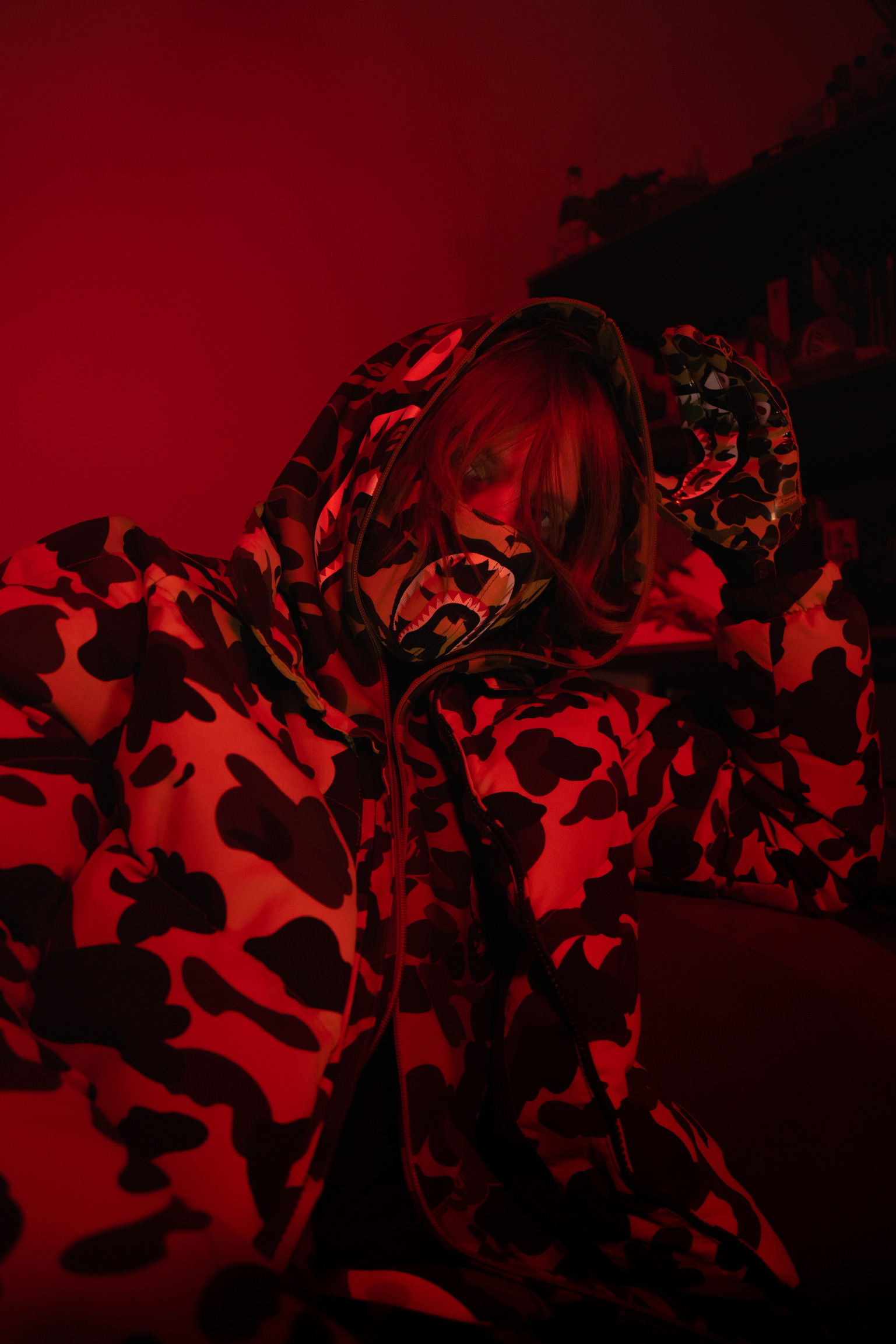 Photo de l'artiste Sixth dans une ambiance très rouge et sombre, il porte une veste camouflage et une capuche